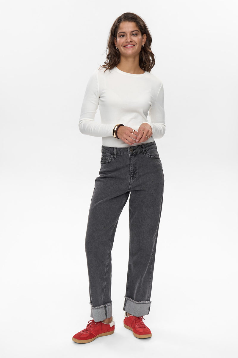 Woman wearing a white long-sleeve shirt, gray jeans, and red shoes on a white background