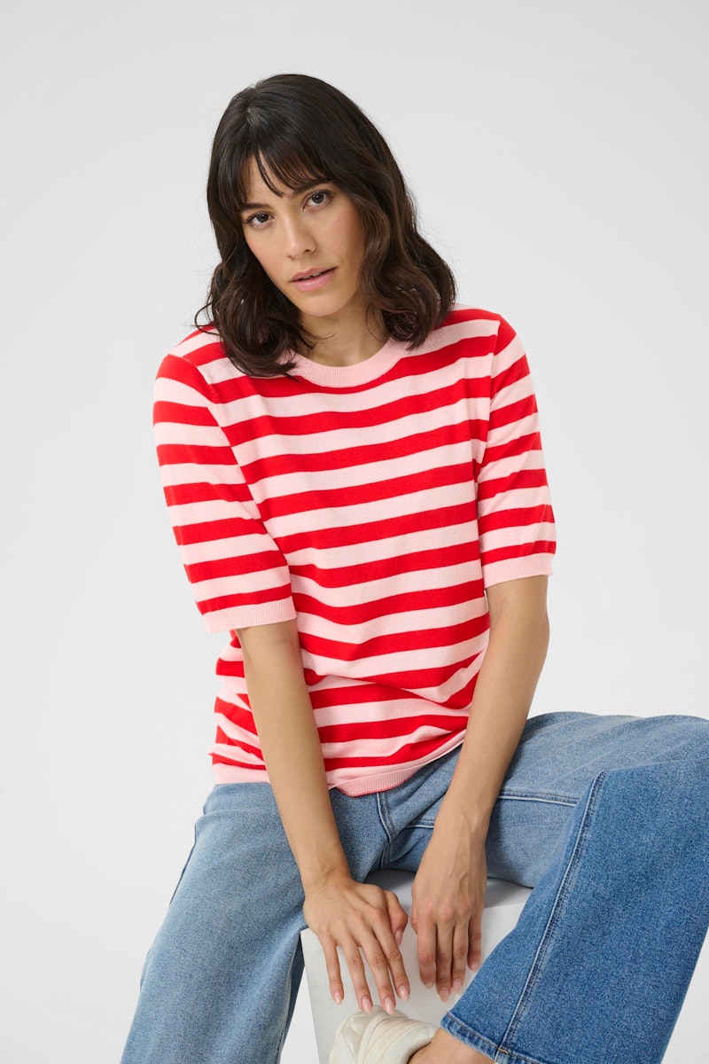 Woman wearing a red and white striped shirt and blue jeans sitting on a white surface.
