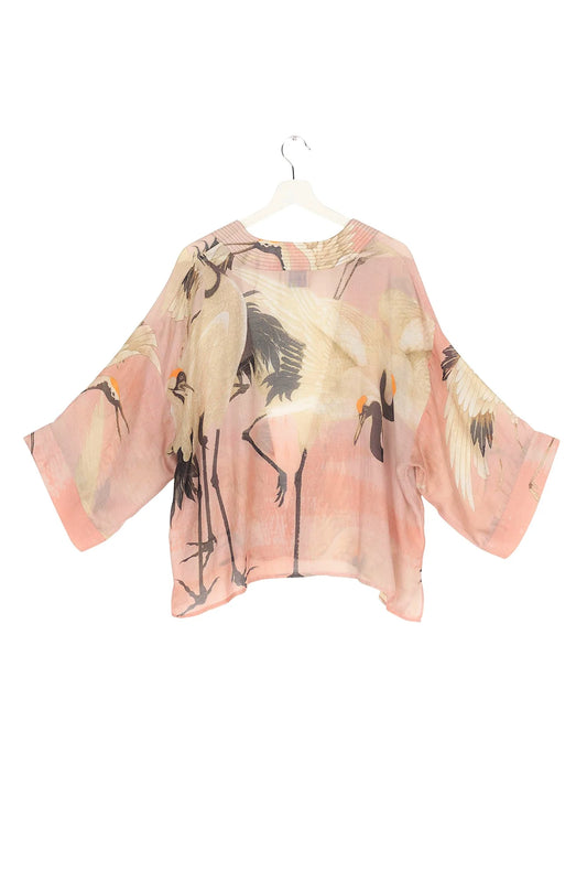 A pink kimono with stork and crane patterns, displayed on a hanger against a white background.