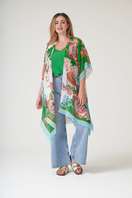 Woman wearing a colourful floral kimono over a green top and blue jeans on a white background