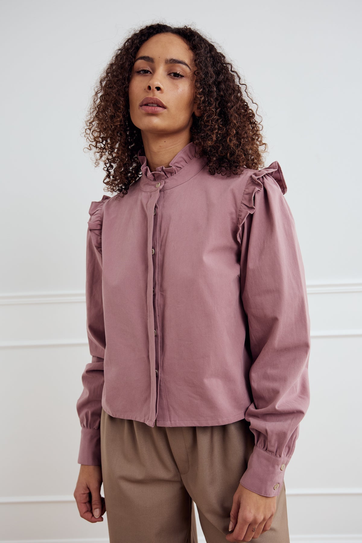 Noella Laina Blouse in Vintage Rose. Woman wearing a pink blouse with ruffled shoulders against a white background