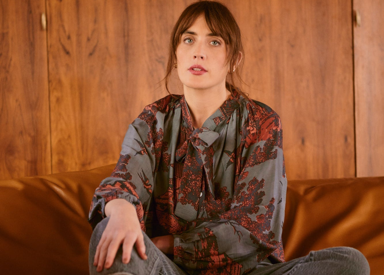 Woman sitting on a brown leather couch against a wooden wall.