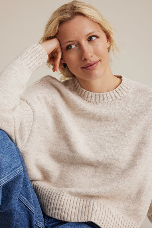 Woman wearing a beige sweater against a neutral background