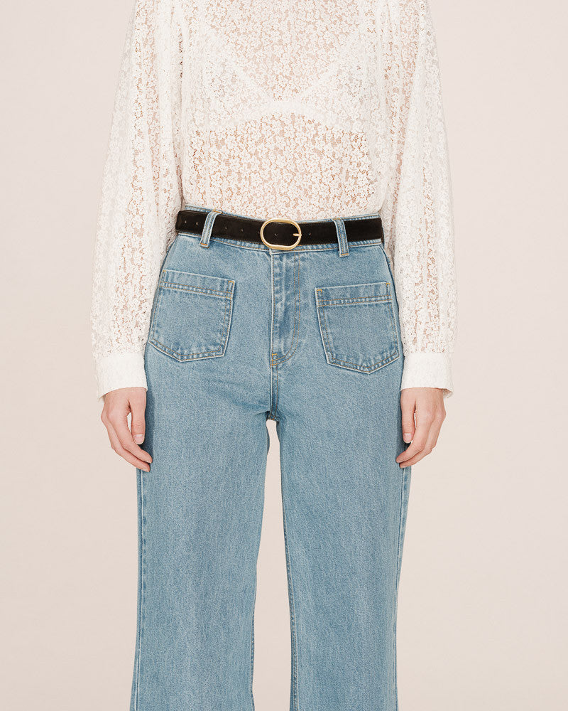 Person wearing light blue jeans with a white lace top on a beige background