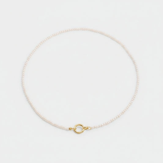 Delicate gold necklace with a small ring pendant on a light gray background