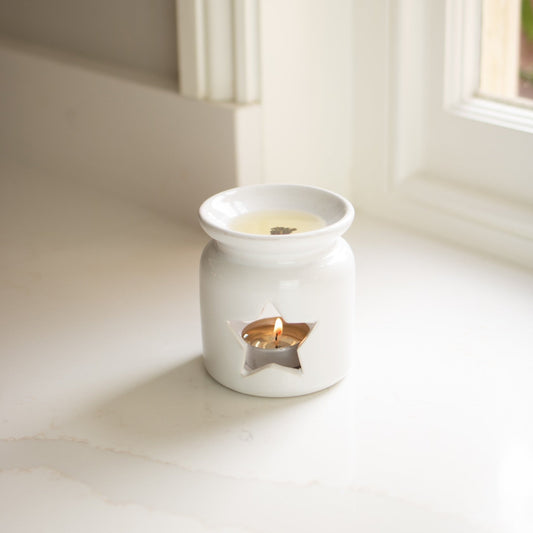 White ceramic wax warmer with a lit candle on a light surface.