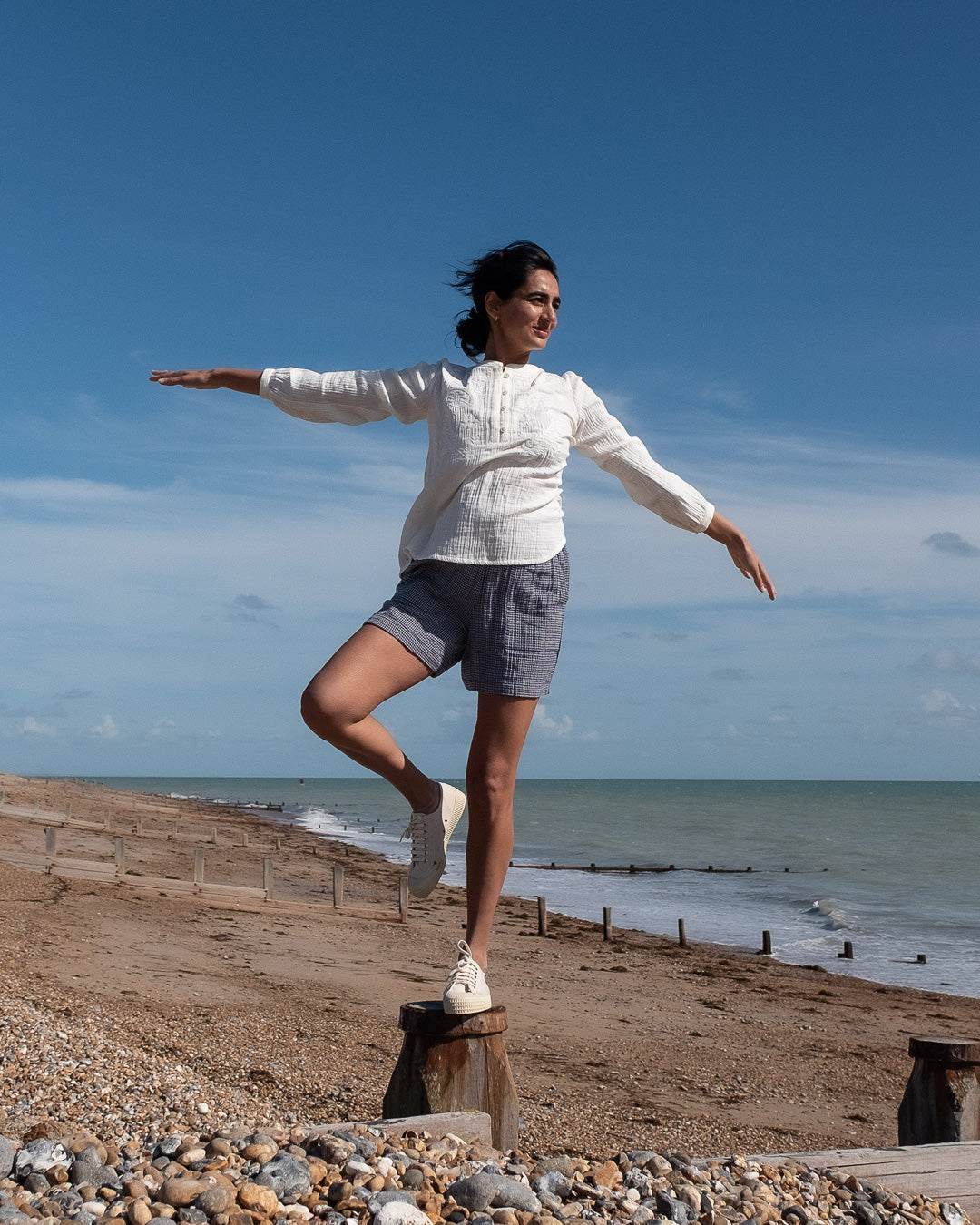 Woman balancing on a log at the beach with ocean and sky in the background