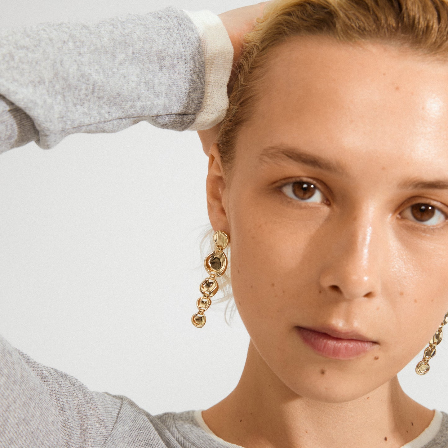 Close-up of a person wearing gold earrings with a neutral background