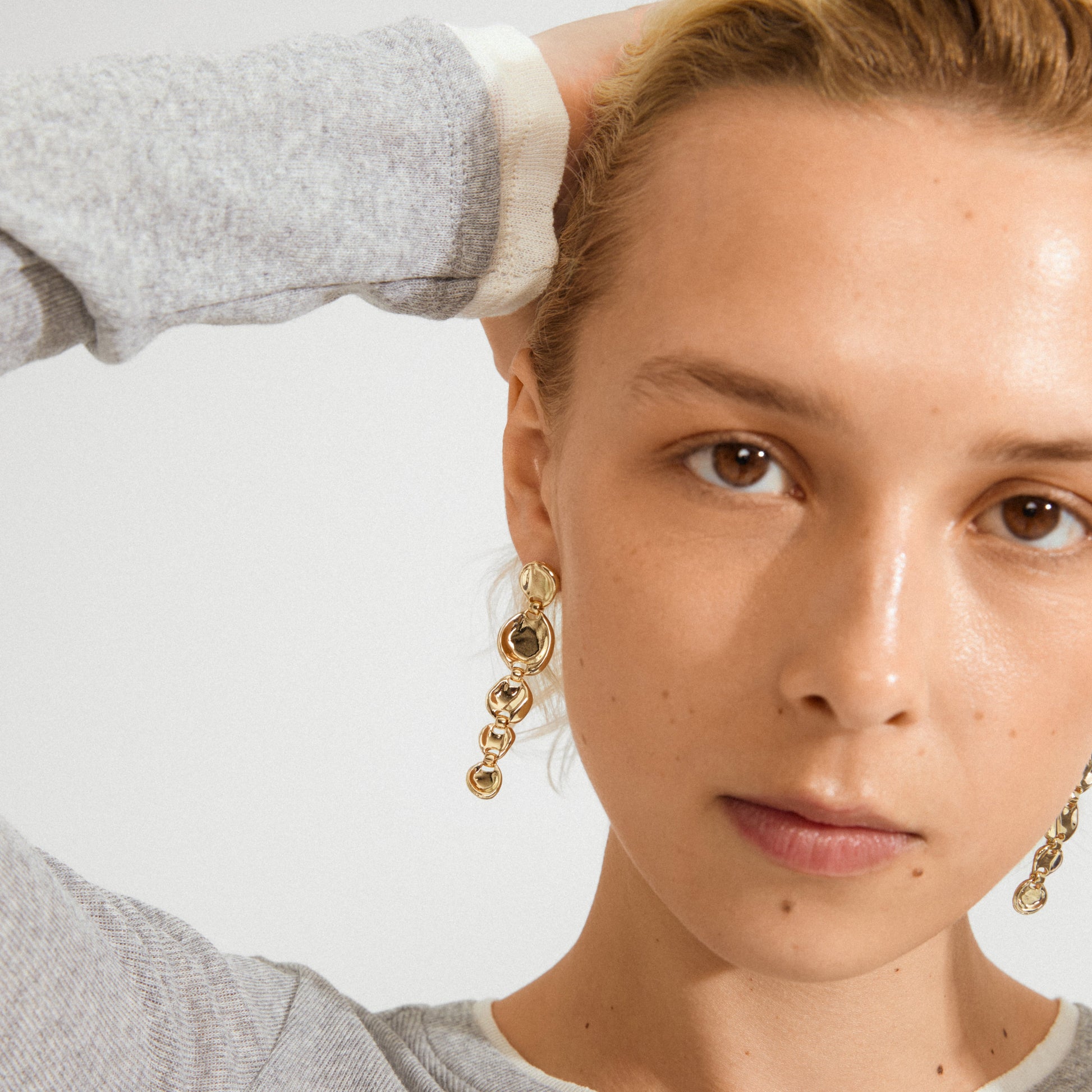 Close-up of a person wearing gold earrings with a neutral background