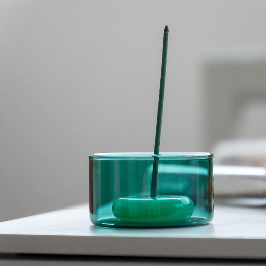 Green glass incense holder with a single incense stick on a neutral background