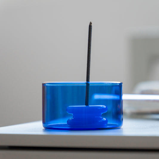 Blue glass incense burner with a single stick on a white surface.