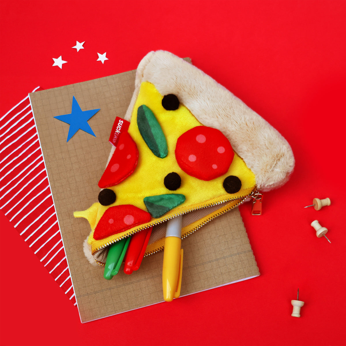 Plush Pizza Zip Pouch - Pizza-shaped pouch on a notebook with push pins against a red background