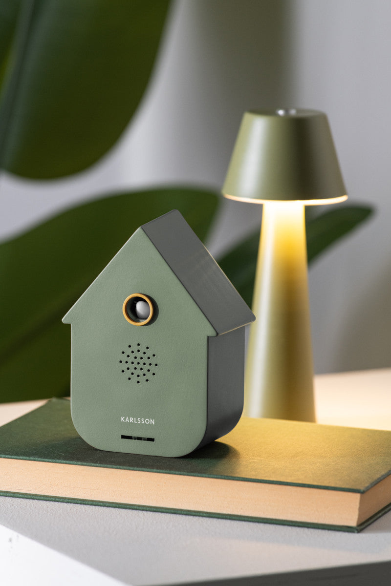 Green house-shaped speaker on a book with a lamp in the background