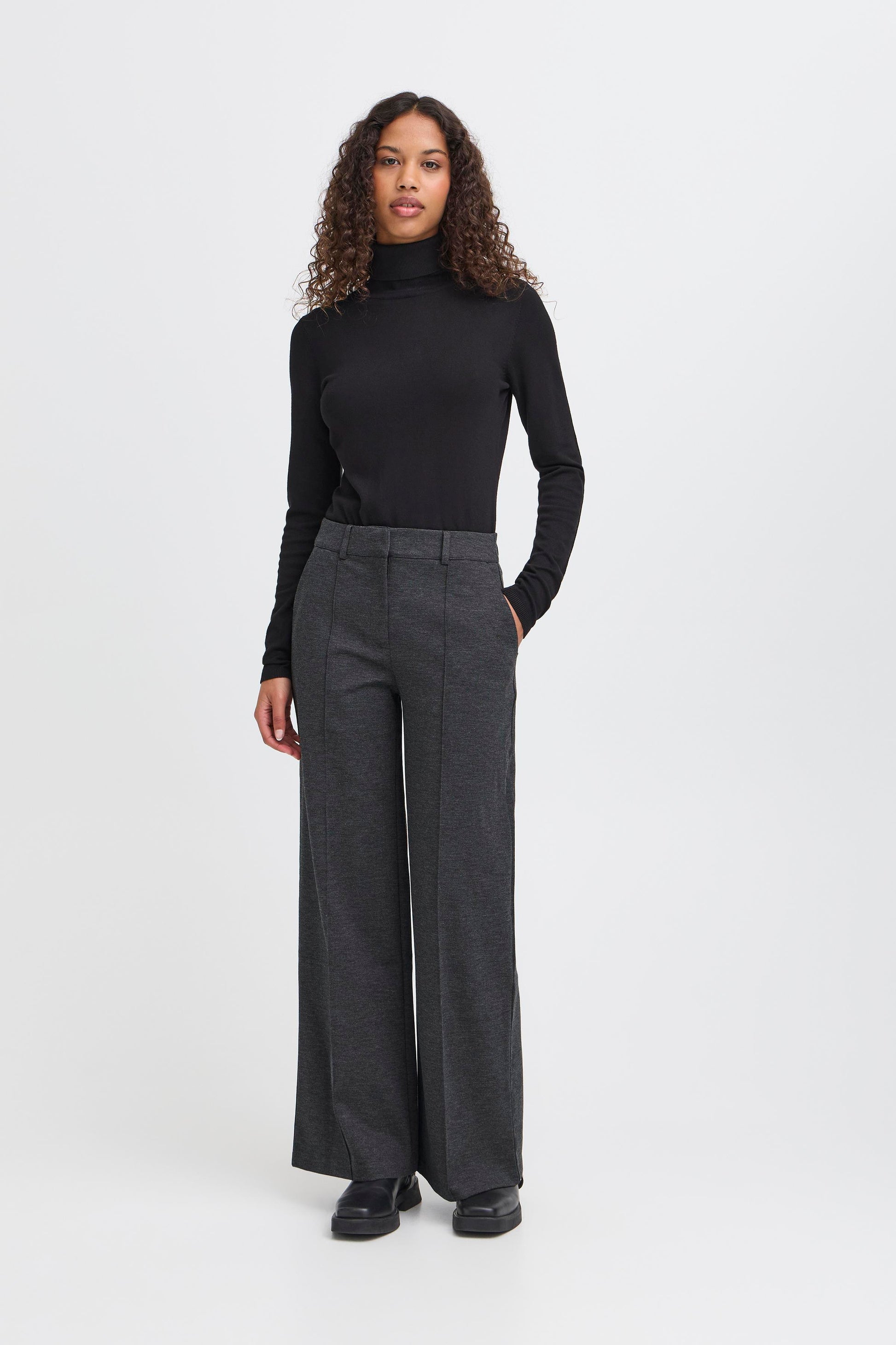 Woman wearing a black turtleneck and gray wide-leg pants on a white background