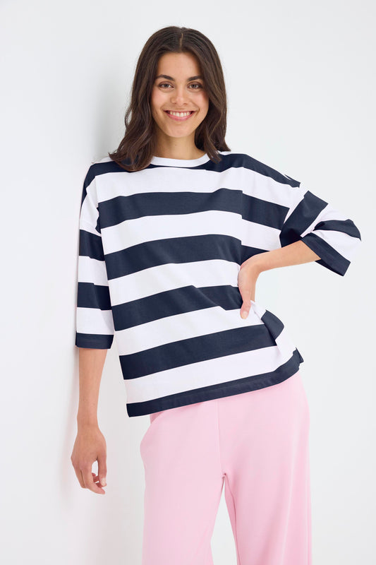 Woman wearing a navy and white striped sweater with pink pants on a white background