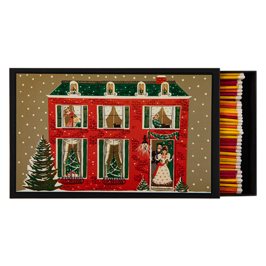 A Christmas-themed matchbox with a red brick house illustration under snow, shown open with colorful matches inside on a white background.