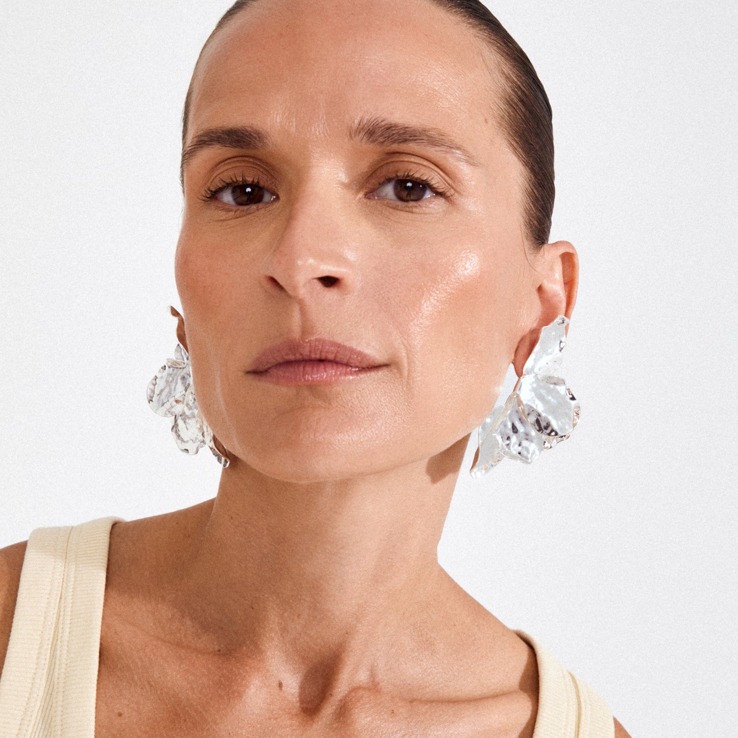 Woman wearing large, sparkling earrings against a plain background