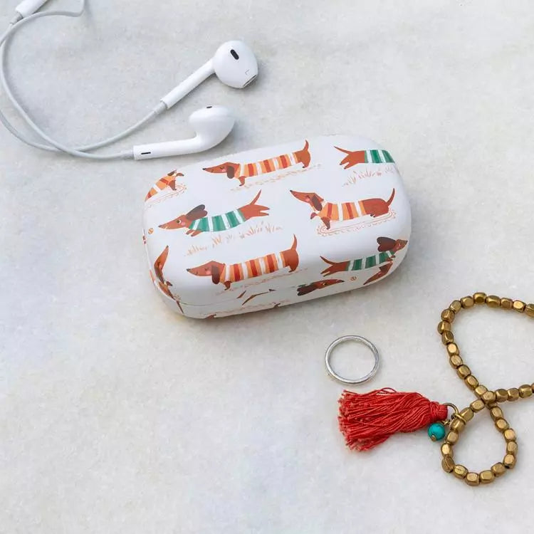 White case with dog pattern, white earphones, ring, and bracelet on a light gray surface