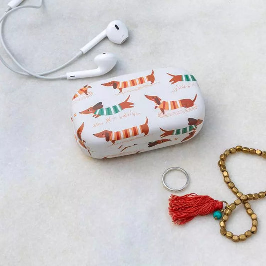 White case with dog pattern, white earphones, ring, and bracelet on a light gray surface