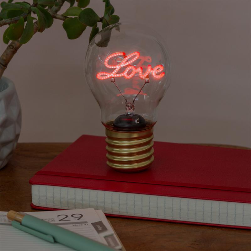 Neon light bulb displaying the word 'Love' on a red notebook with a plant and pen in the background.