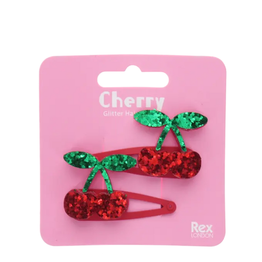 Packaged cherry-shaped hair clips with green and red glitter on a pink background, featuring the brand 'Rex London'.