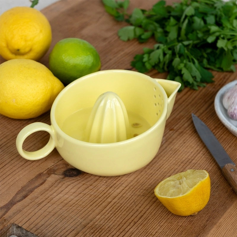Rex London Ceramic lemon juicer - Yellow - Yellow manual juicer on a wooden surface with lemons, limes, and a knife.