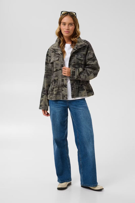Kaffe Lilana Cargo Jacket in Camo - a woman modeling a cropped camouflage jacket over a white t-shirt and blue jeans, standing against a light grey studio background.
