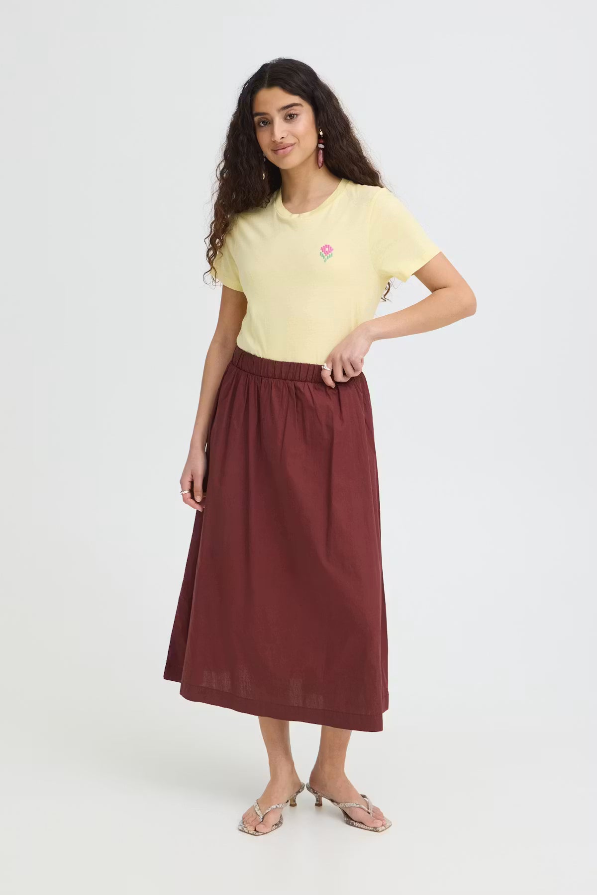 Woman wearing a yellow t-shirt and maroon skirt on a white background