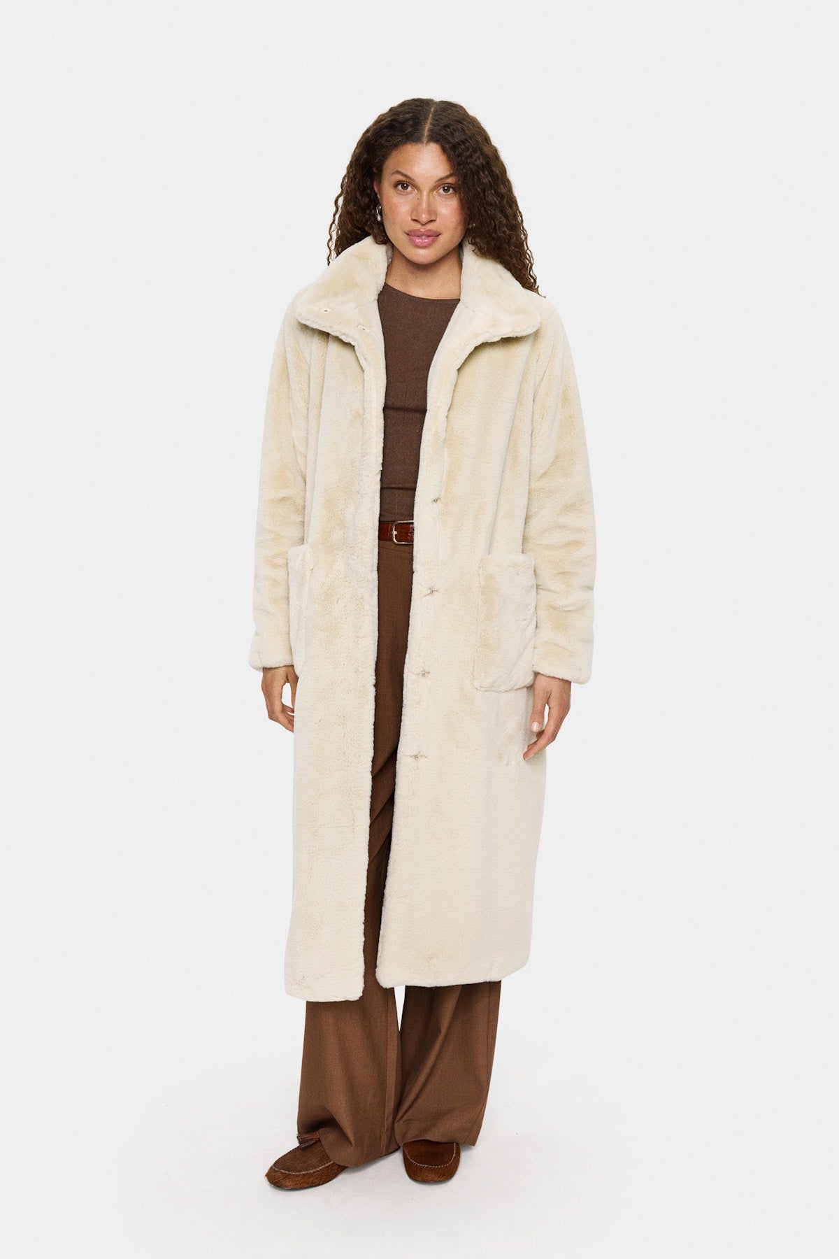 Woman wearing a long cream coat over a brown outfit on a white background
