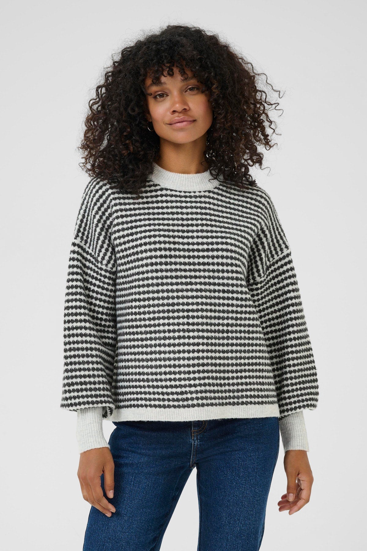 Person wearing a black and white checkered sweater with blue jeans on a plain background