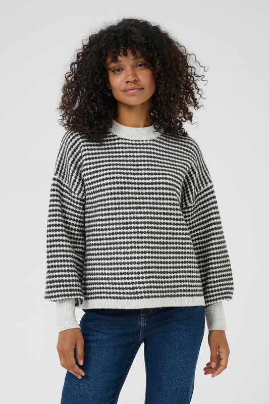 Person wearing a black and white checkered sweater with blue jeans on a plain background