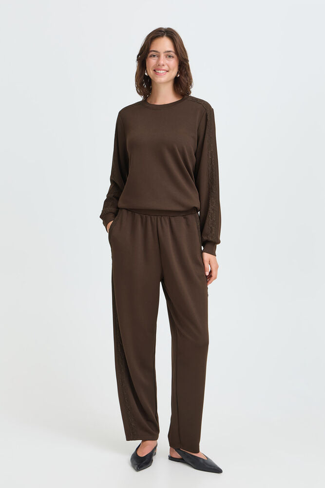 A woman modeling a dark brown long-sleeve top and matching wide-leg pants set against a plain light gray studio background.