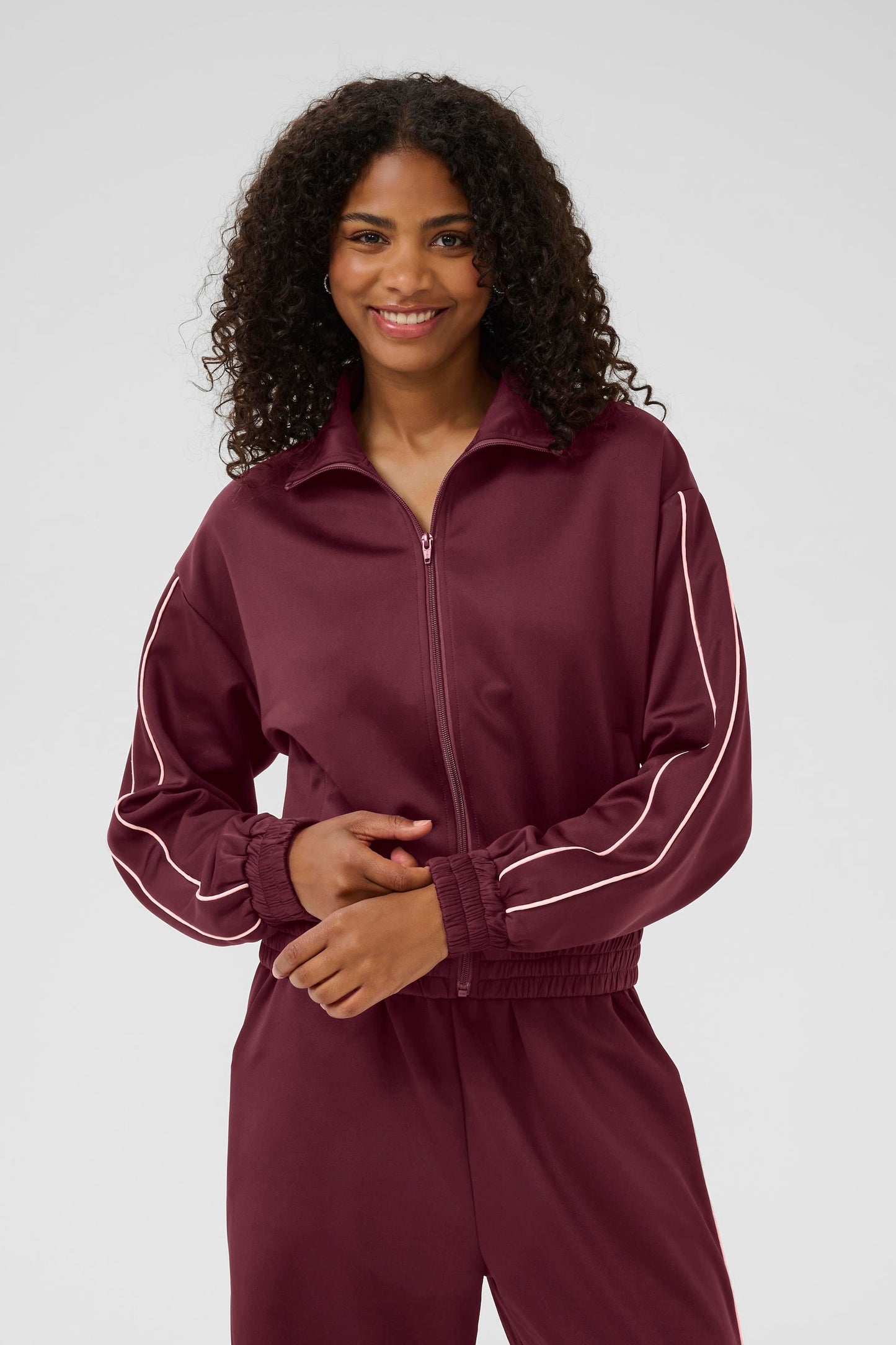 Woman wearing a maroon tracksuit with white stripes on a plain background