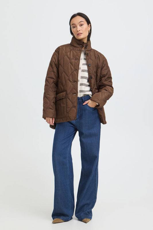 Fransa Agate Jacket in Rain Drum - A model stands against a light grey studio background wearing a brown quilted jacket over a striped knit top and blue wide-leg jeans.