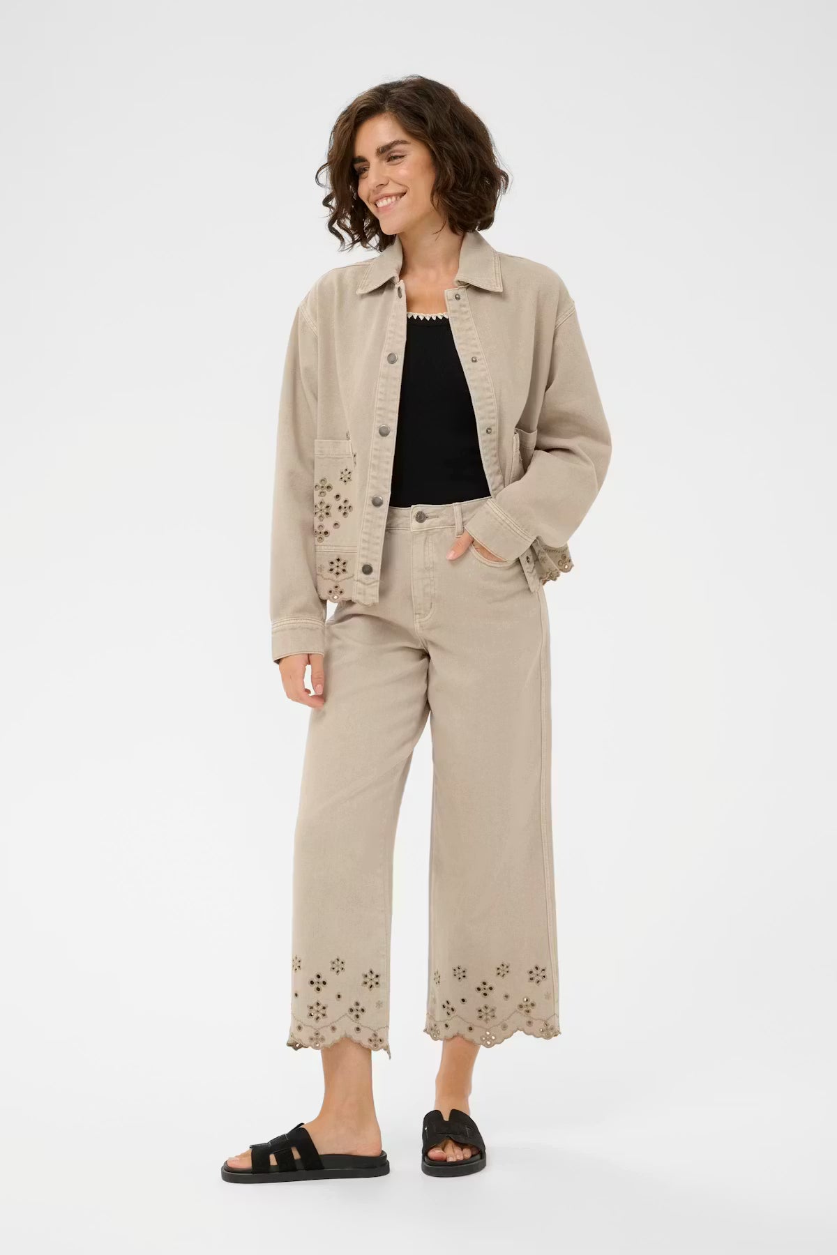 Woman wearing a beige jacket and pants with floral embroidery on a white background