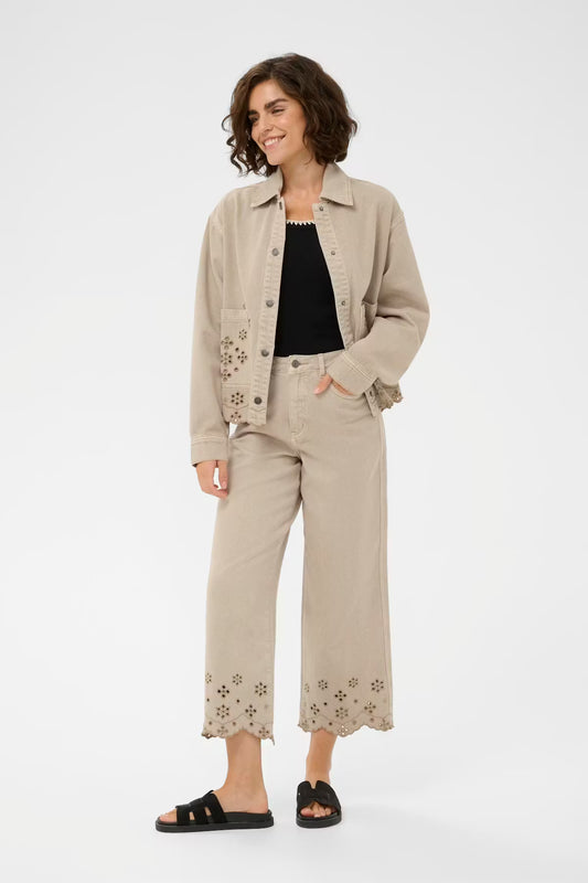 Woman wearing a beige jacket and pants with floral embroidery on a white background