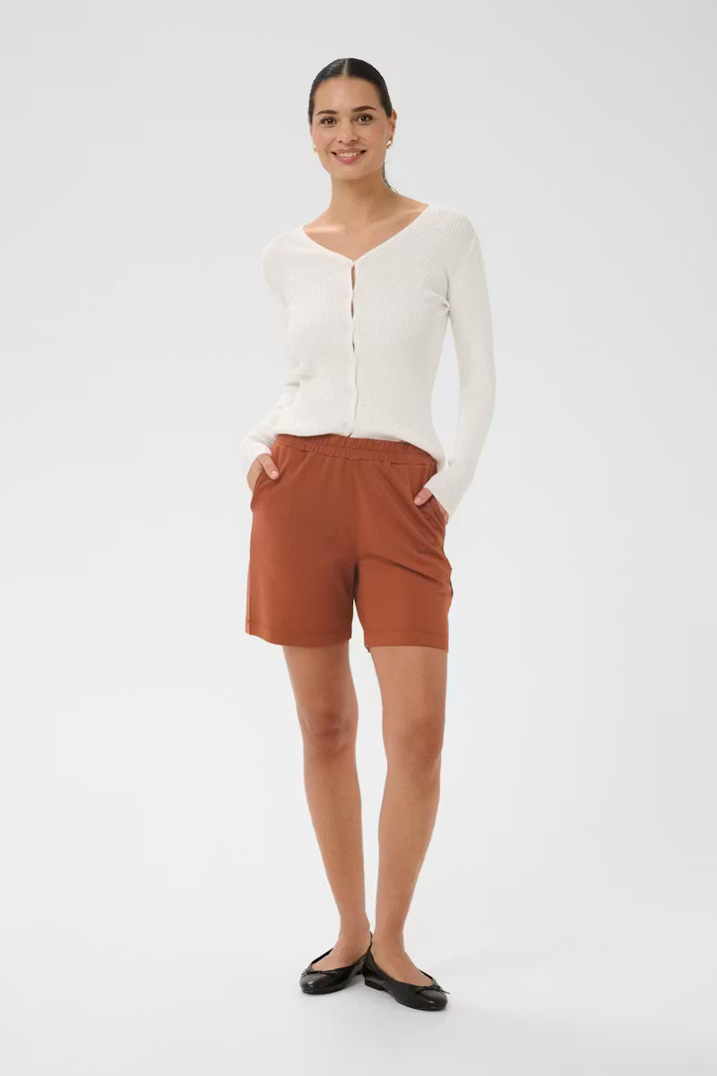Woman wearing a white cardigan and brown shorts on a white background