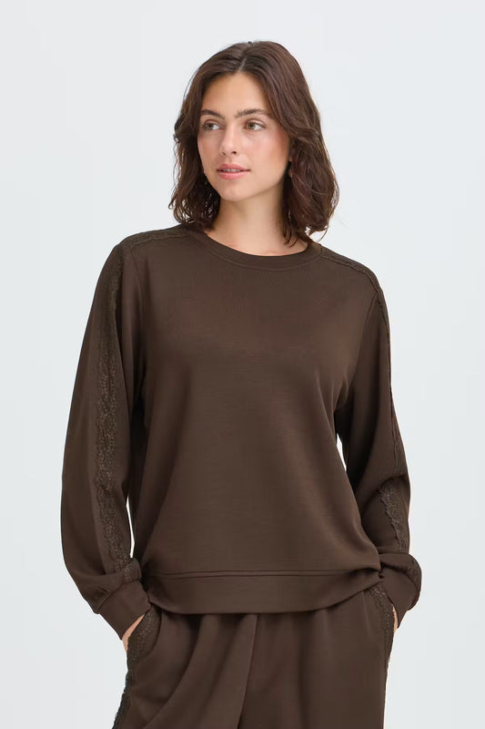 Fransa Aurora Sweatshirt in Mole - A woman wearing a dark brown crewneck sweatshirt with textured lace detailing on the sleeves, paired with matching brown pants, against a light grey studio background.