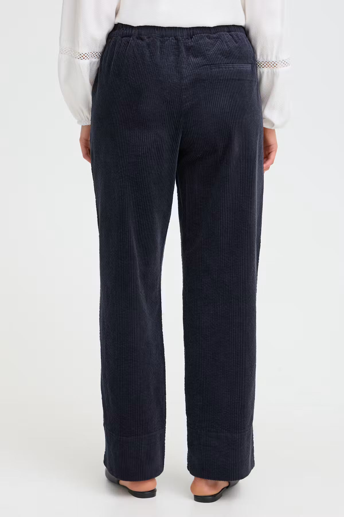 A person shown from the back wearing dark navy corduroy wide-leg trousers, a white blouse, and black flat shoes against a plain white studio background. Fransa Salomi Pant in Salute