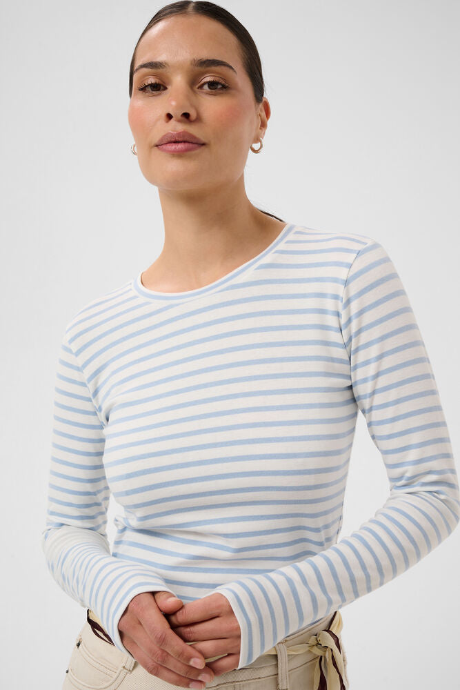 KAFFE Plain Stripe T-Shirt in Chalk White and Blue Fog Stripe - A woman wearing a light blue and white horizontally striped long-sleeve crewneck top, paired with beige pants, against a plain light grey studio background.