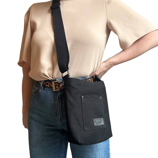 Person wearing a black crossbody bag with a beige shirt and blue jeans on a white background