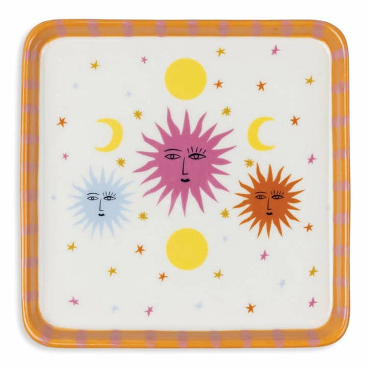 A square decorative plate with rounded corners, featuring a whimsical celestial design of three suns and crescent moons with faces on an off-white background, surrounded by small stars. The plate has a thick orange border with pink stripes.