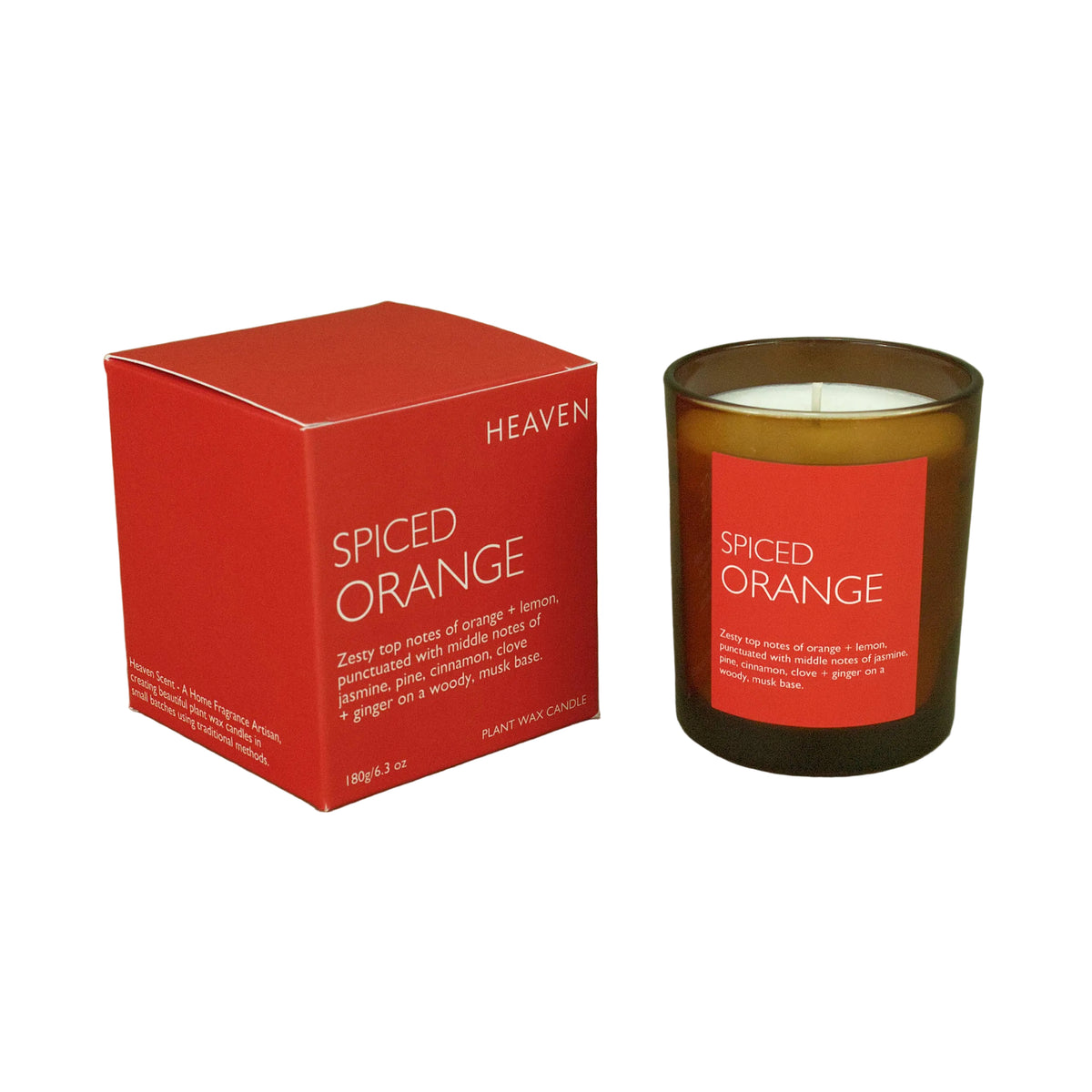 A spiced orange scented candle in an amber glass jar next to its red packaging box, set against a solid olive green background. The box features the brand name 'Heaven' and the scent 'Spiced Orange'.