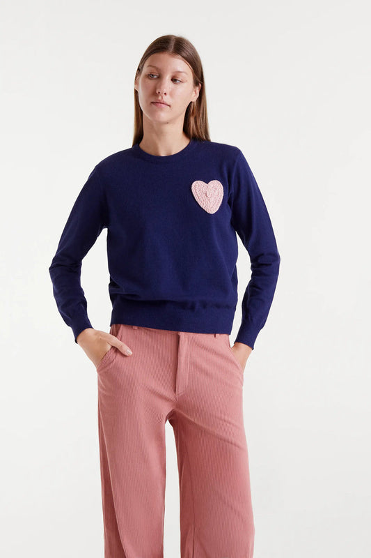 Woman wearing a navy sweater with a pink heart design and pink pants on a white background