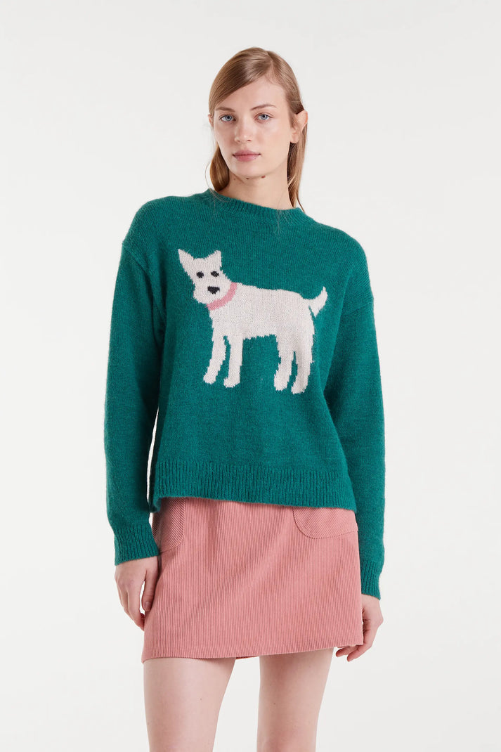 Woman wearing a green sweater with a dog design and a pink skirt on a white background