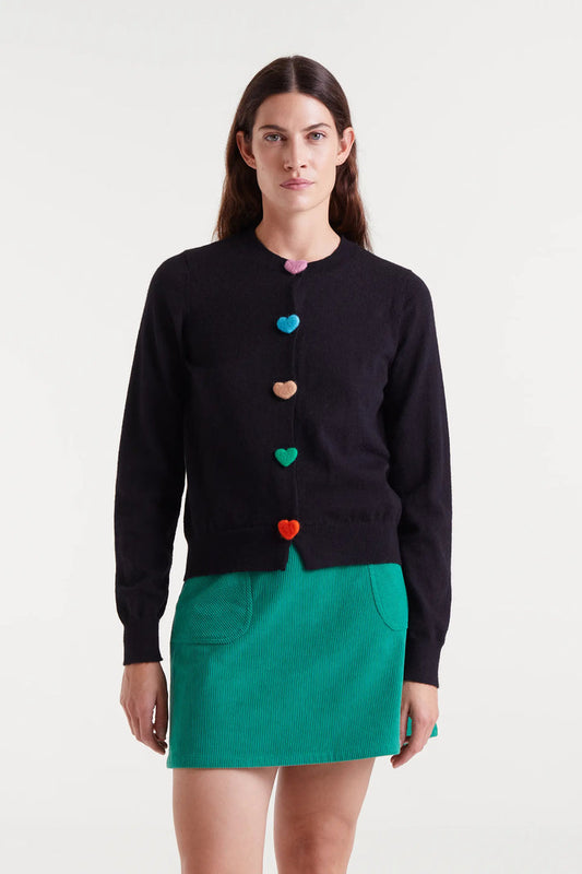 Woman wearing a black cardigan with colorful heart buttons and a green skirt on a white background