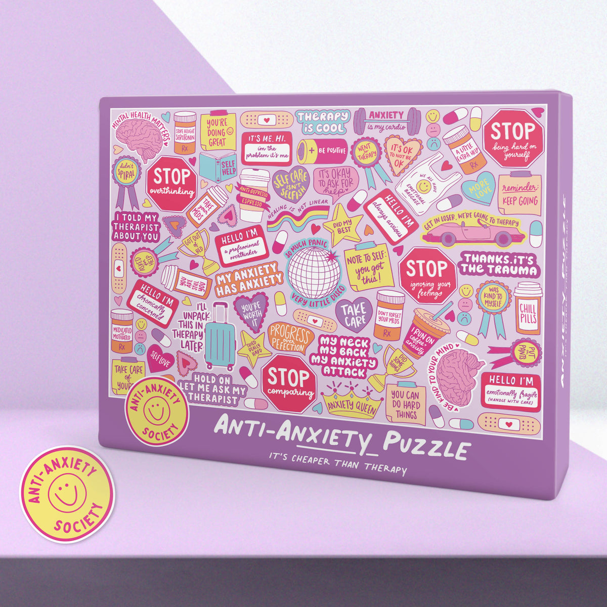 A purple rectangular jigsaw puzzle box labeled 'ANTI-Anxiety PUZZLE' with a dense collage of pastel and bright stickers, signs, and therapy-themed illustrations on the front. A round yellow sticker badge reading 'ANTI-Anxiety SOCIETY' appears in the lower left on a lavender background.