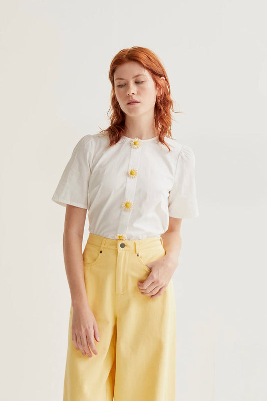 Woman wearing a white blouse with yellow buttons and yellow pants on a plain background