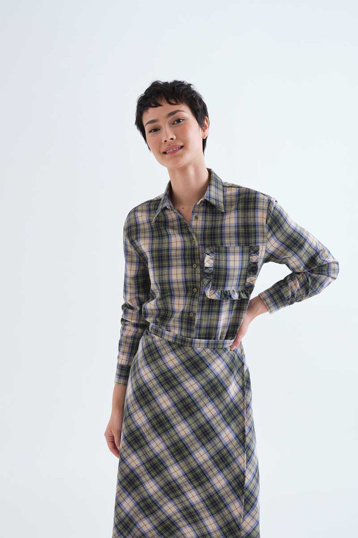 A model wearing a long-sleeve plaid shirt and skirt in gray, beige, and white, standing against a plain light gray background.