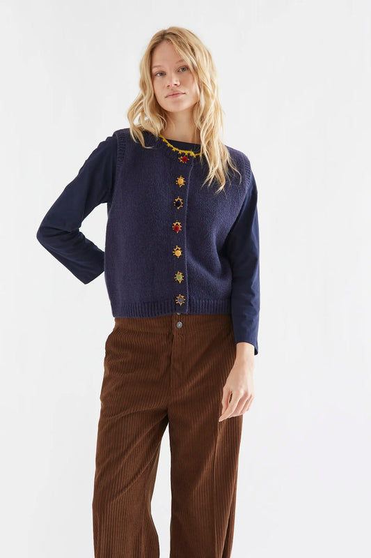 Compania Fantastica Navy Blue Knit Vest with Multicolored Velvet Buttons - A woman modelling a navy blue knit cardigan with colourful decorative buttons and brown corduroy pants against a plain white studio background.